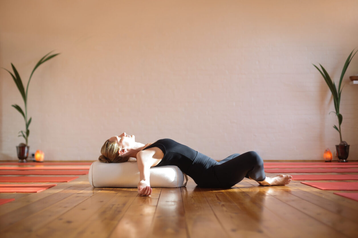 Young woman practicing yoga at home during self-isolation under covid-19 situation with head pillow under morning sunlight